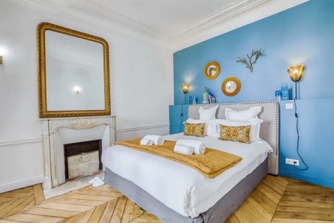 Elegant bedroom with white bedding, gold accents, and a blue feature wall in Gare du Nord Apartments.