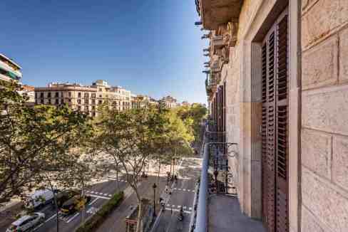 View from a balcony overlooking Barcelona's Gran Via with city buildings and trees.