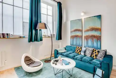 Bright and stylish living room with a blue sofa, abstract artwork, and large windows in Rue Lallier.