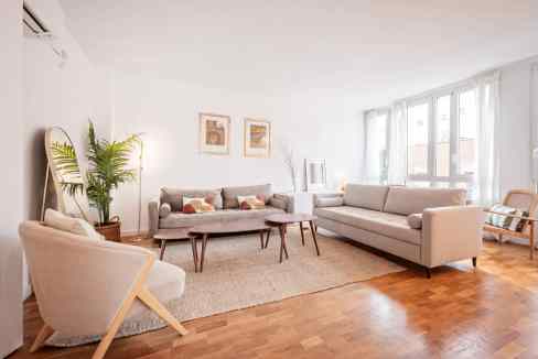 Spacious living room with large windows, neutral furniture, and natural light.