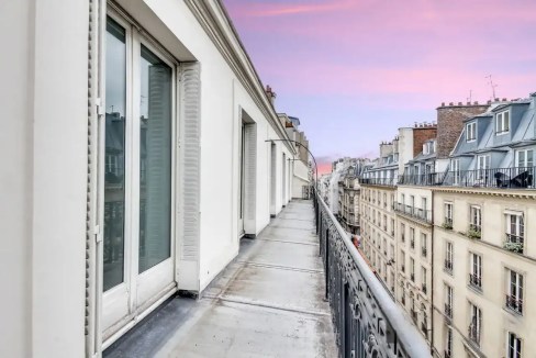Balcony view from Rue de Ponthieu apartments with Paris cityscape and colorful sunset sky.