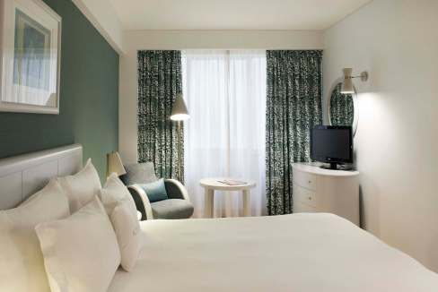 Modern hotel room with a large bed, armchair, and TV at Lisbon Avenida Aparthotel.
