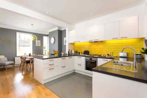 Modern kitchen with white cabinets and yellow tile backsplash at Bishopgate Street Apartments.