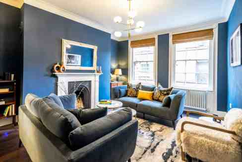 Stylish living room with blue walls, large windows, and modern furniture in York Castlegate Apartmen.