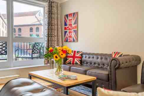Bright living room featuring Union Jack cushions and artwork, with a view of Umbrella Alley Apartmen.