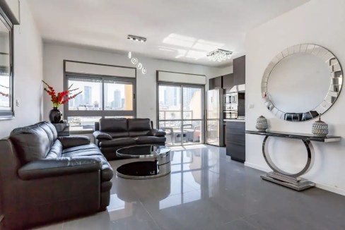 Modern living room with black leather sofas and city views in Hakovshim Street Apartments.