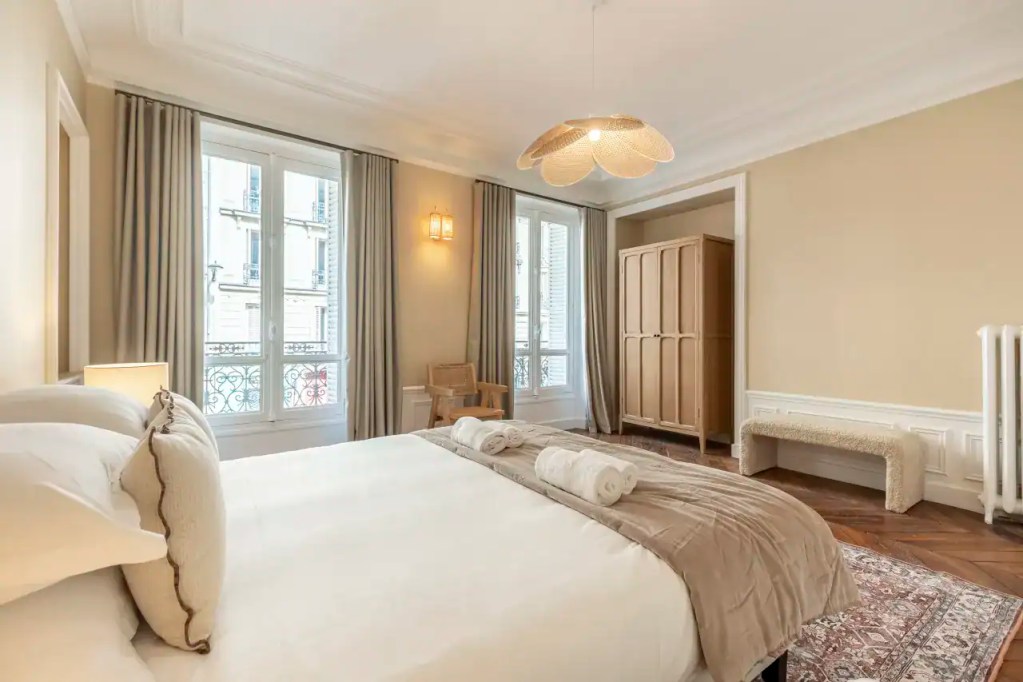 Elegant Parisian apartment bedroom with large windows and classic decor.