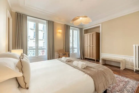 Elegant Parisian apartment bedroom with large windows and classic decor.