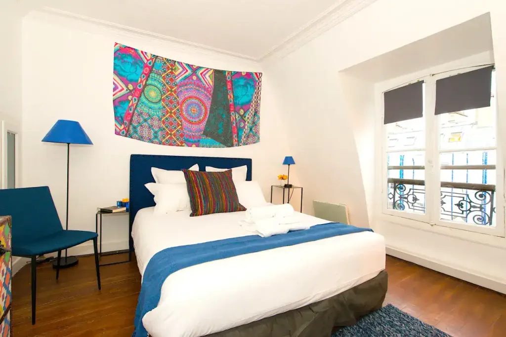 Cozy bedroom featuring vibrant artwork, modern decor, and natural light at Rue Saint-Honore Apartmen.