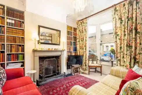 Charming Victorian-style living room featuring vintage furniture, floral curtains, and a fireplace,.