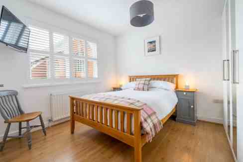 Bright bedroom with wooden bed, large window, and cozy decor at Shipton St House.