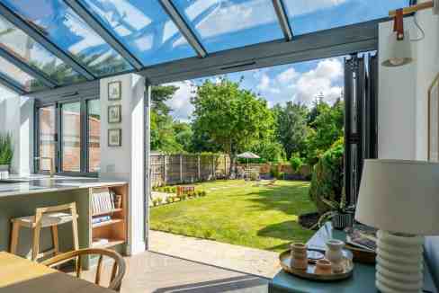 Sunroom opening to lush backyard with trees and lawn.