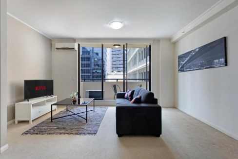 Living room with city views at North Sydney Napier Apartments. Modern furniture and large windows in.