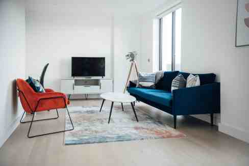 Bright, minimalist living room featuring a blue sofa, red armchair, and large windows.