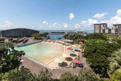 View of Darwin Waterfront with beach, umbrellas, and surrounding buildings.