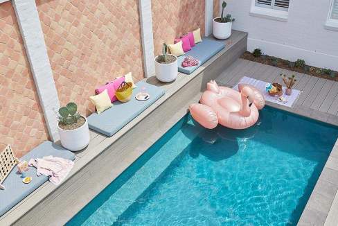 Outdoor swimming pool with lounge seating and decorative pillows at Sydney Chippendale Aparthotel.
