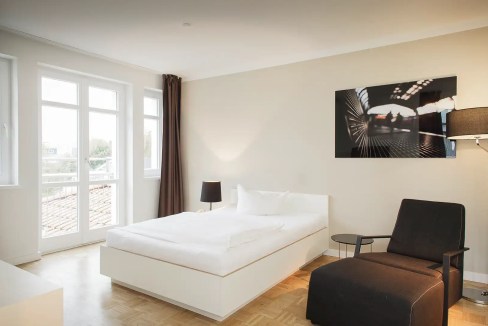 Bright and spacious bedroom featuring large windows, contemporary decor, and comfortable seating at.