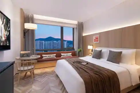 Hotel room with city view, modern decor, and comfortable bedding at Sanya Yazhou Bay Aparthotel.
