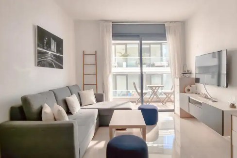 Bright living room with sofa, TV, and balcony view in Tel Aviv apartment.