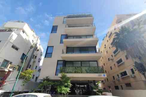 Apartment building with multiple balconies on Shalom Aleichem Street, surrounded by greenery and nei.