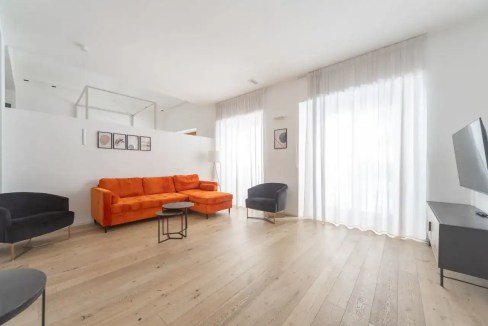 Modern living room with orange sofa and black armchairs in Porta Venezia Apartments.