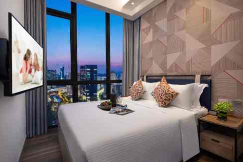 Comfortable bedroom with large windows, stylish decor, and cityscape backdrop.