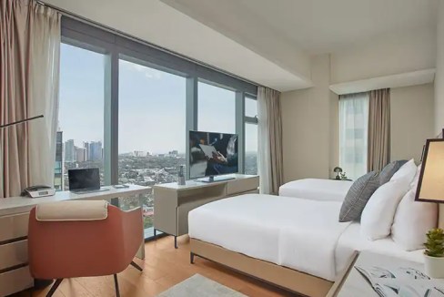 A spacious hotel room at Manila Makati Avenue Aparthotel featuring large windows, contemporary decor.