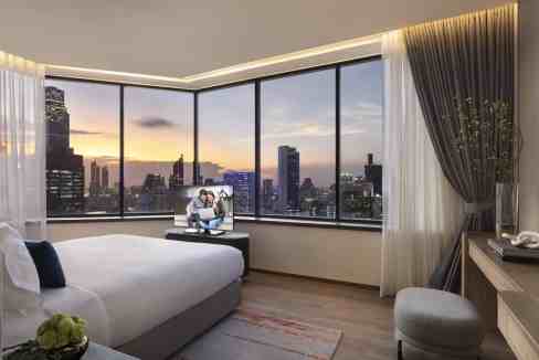Bright hotel room with panoramic city views of Bangkok at sunset.
