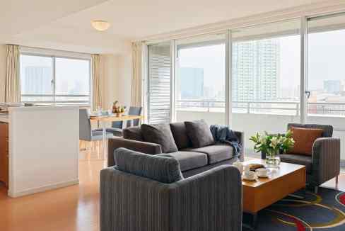 Bright living room in Tokyo Shirokanedai aparthotel featuring large windows and cityscape views.