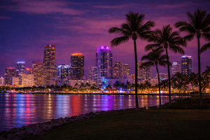 Brightly lit Miami cityscape with colorful skyscrapers and reflections on the water at dusk.