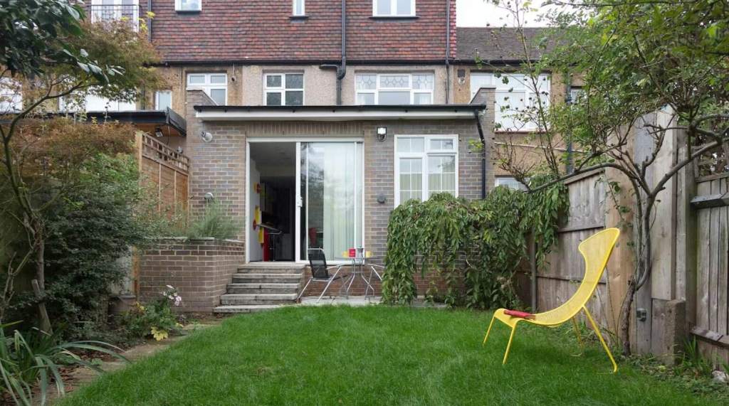 Modern backyard garden with green lawn and yellow chair in Wood Green.