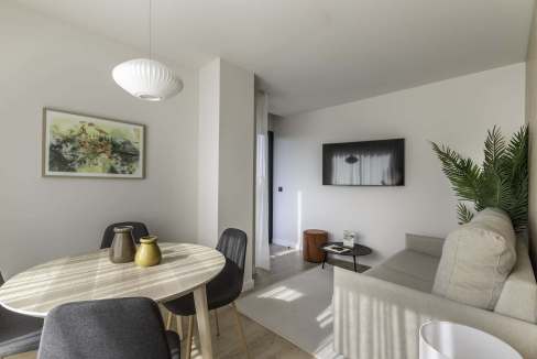 Contemporary living room featuring a dining table, stylish chairs, a sofa, and a wall-mounted TV in.