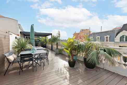 Rooftop terrace with outdoor dining area, potted plants, and city views on a sunny day.