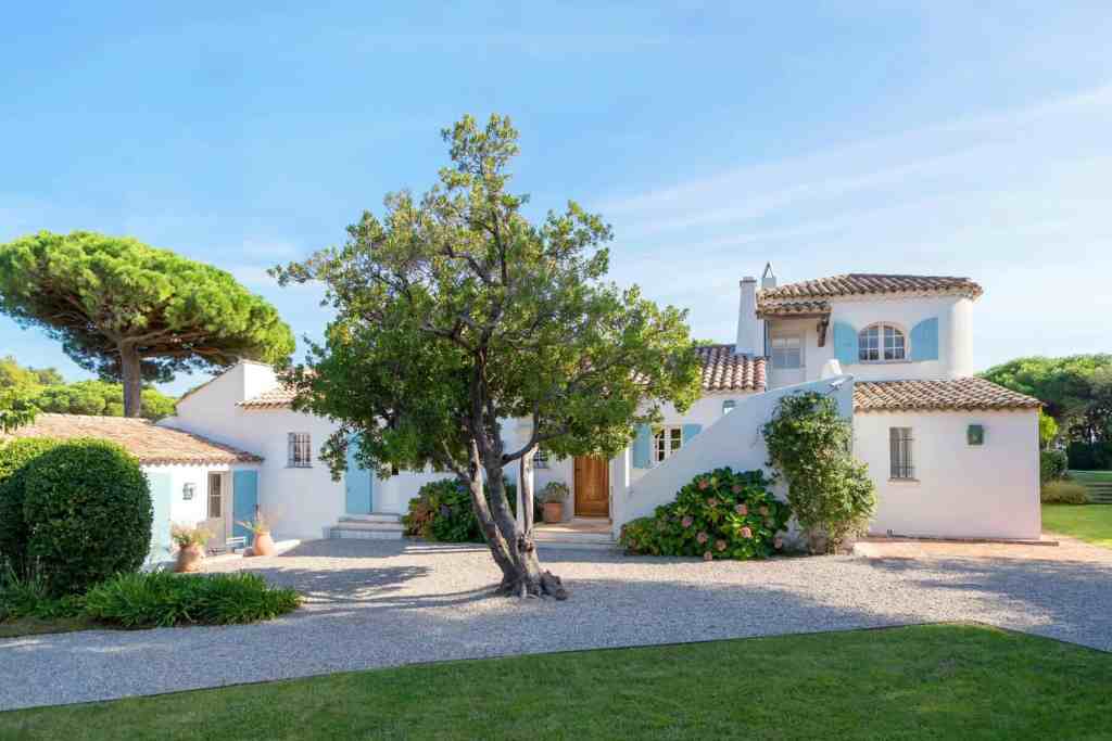 Beautiful Mediterranean-style villa with lush greenery and clear blue sky backdrop.