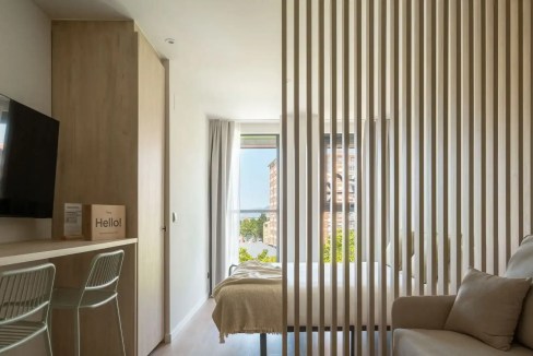 Modern bedroom with wooden slat room divider and large window, bright and airy interior design.