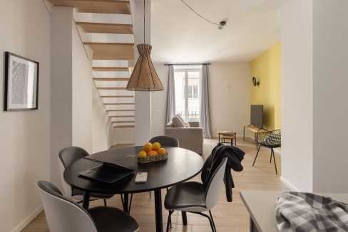 Bright living room with dining space, featuring a round table, stylish chairs, and a cozy seating ar.