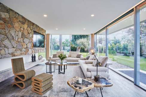 Spacious modern living room with large glass windows, stone wall, and contemporary furniture for sty.