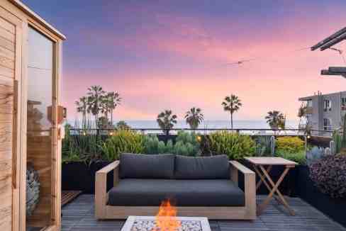 Rooftop terrace with ocean view, modern furniture, and lush greenery during sunset.