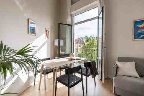 Bright modern apartment with balcony overlooking city skyline and greenery.