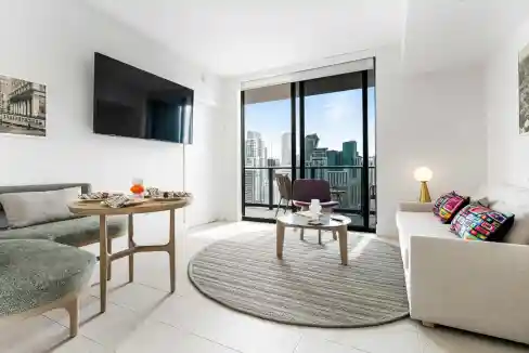 Bright modern living room with city skyline view, minimalist decor, and large glass doors.