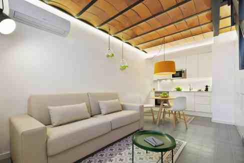Modern living room with minimalist decor, white sofa, wooden ceiling, and contemporary lighting fixt.