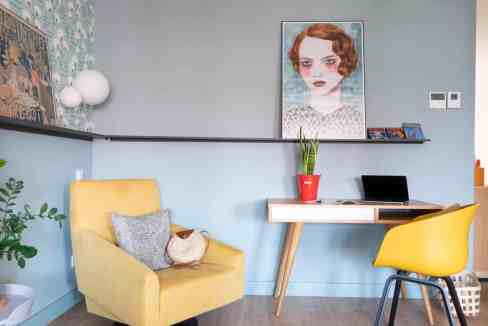 Home office with yellow chair, artwork, and plants for a vibrant workspace.