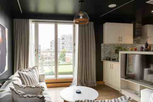 A modern living room with a balcony, featuring minimalist decor, a sofa, and a view of the cityscape.