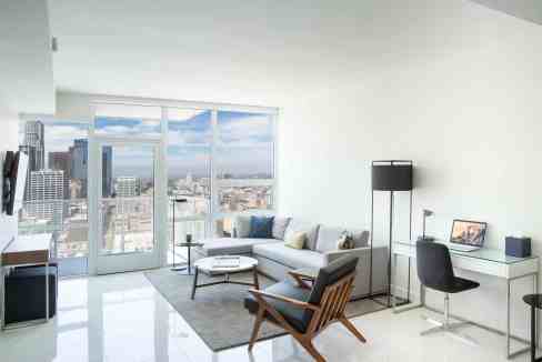 Bright urban living room with floor-to-ceiling windows showcasing cityscape and contemporary furnitu.