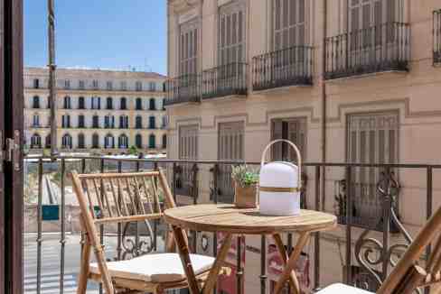 Balcony with wooden table, chairs, and potted plants overlooking urban buildings.