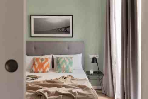 Cozy bedroom with green walls, modern decor, and a framed black-and-white bridge photo.