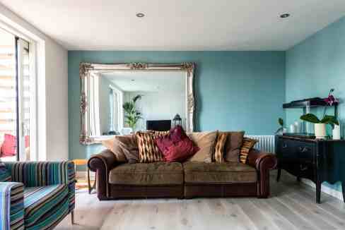 Bright and airy living room featuring a brown sofa, colorful cushions, and a large mirror on a turqu.