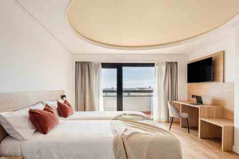 Hotel room with large window overlooking city skyline, featuring clean design and neutral tones.