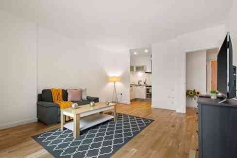 Spacious living room with white walls, gray sofa, coffee table, and wooden flooring.