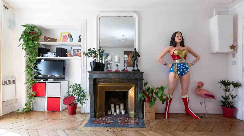 Bright living room with fireplace, plants, and a woman in Wonder Woman costume.